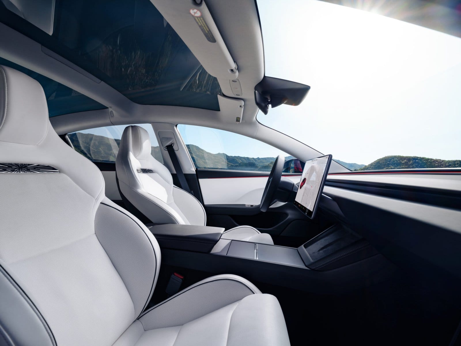 Interior view of the Tesla Model 3 electric vehicle, showcasing white sport seats, a panoramic glass roof, and a minimalist dashboard.