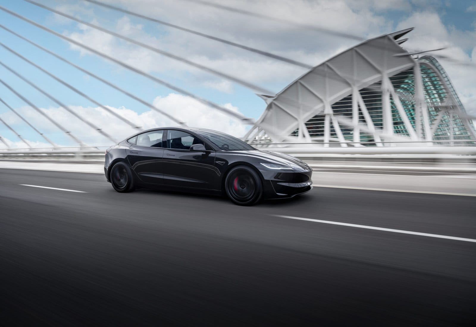 A black Tesla Model 3 electric vehicle in motion on an urban highway, passing a modern cable-stayed bridge with a futuristic architectural design.