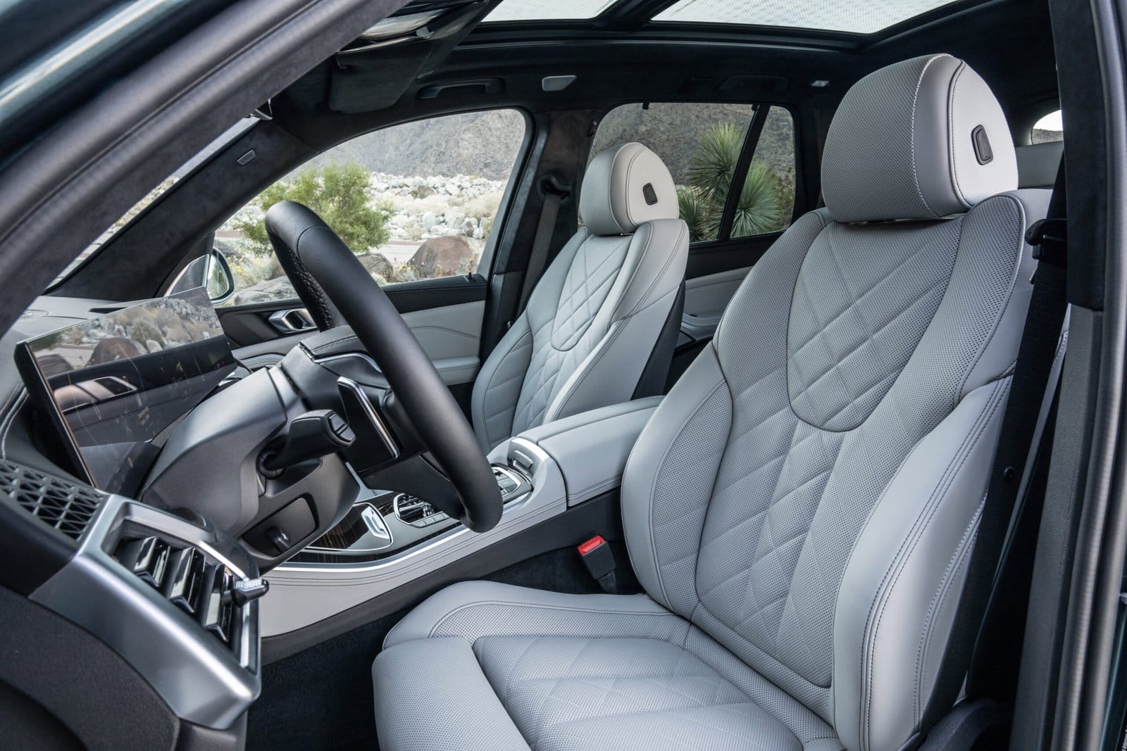 Quilted leather front seats inside a BMW X5 Plug-in Hybrid electric vehicle, with a view of the dashboard and panoramic roof.