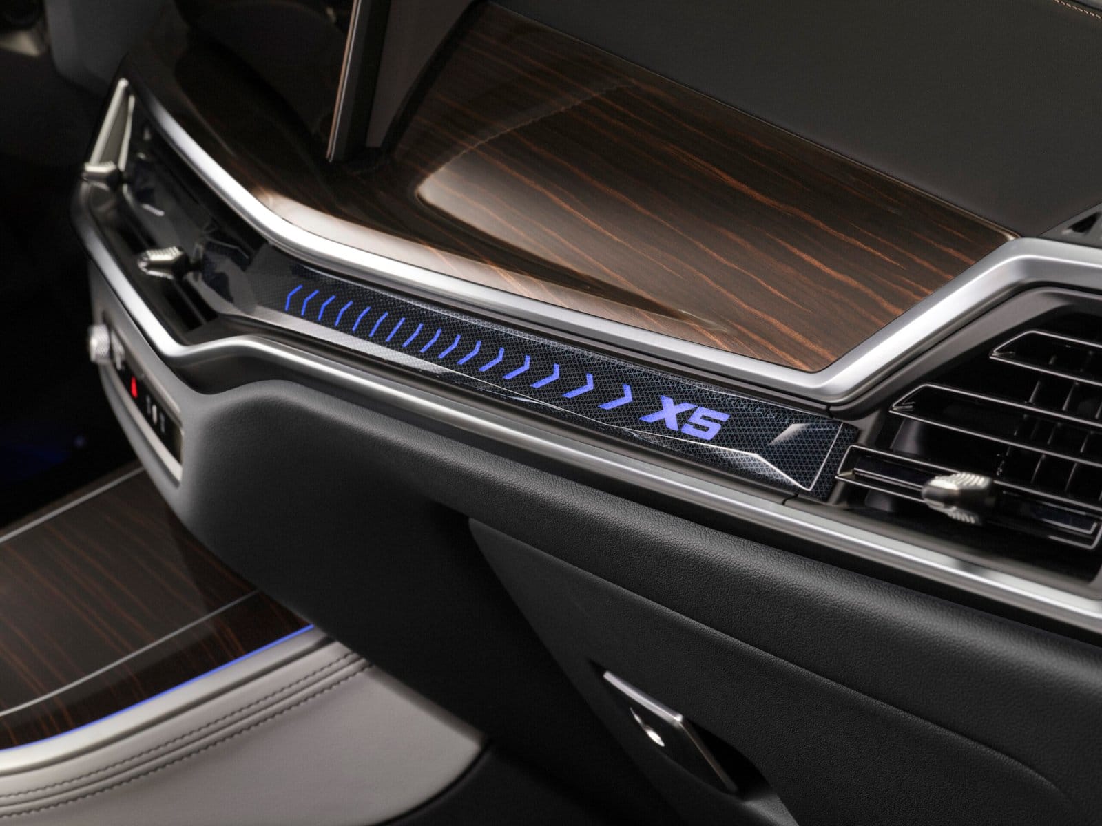 Illuminated X5 badge and blue ambient lighting strip on the dashboard of the BMW X5 Plug-in Hybrid electric vehicle, with wood grain panel.