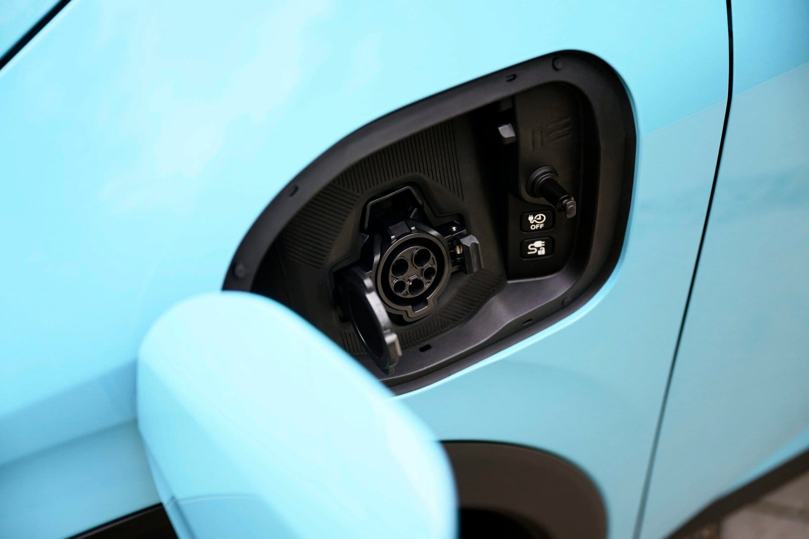 Detailed view of the open charging port on a blue Nissan Leaf electric car, showing the connector interface and charging lock switch