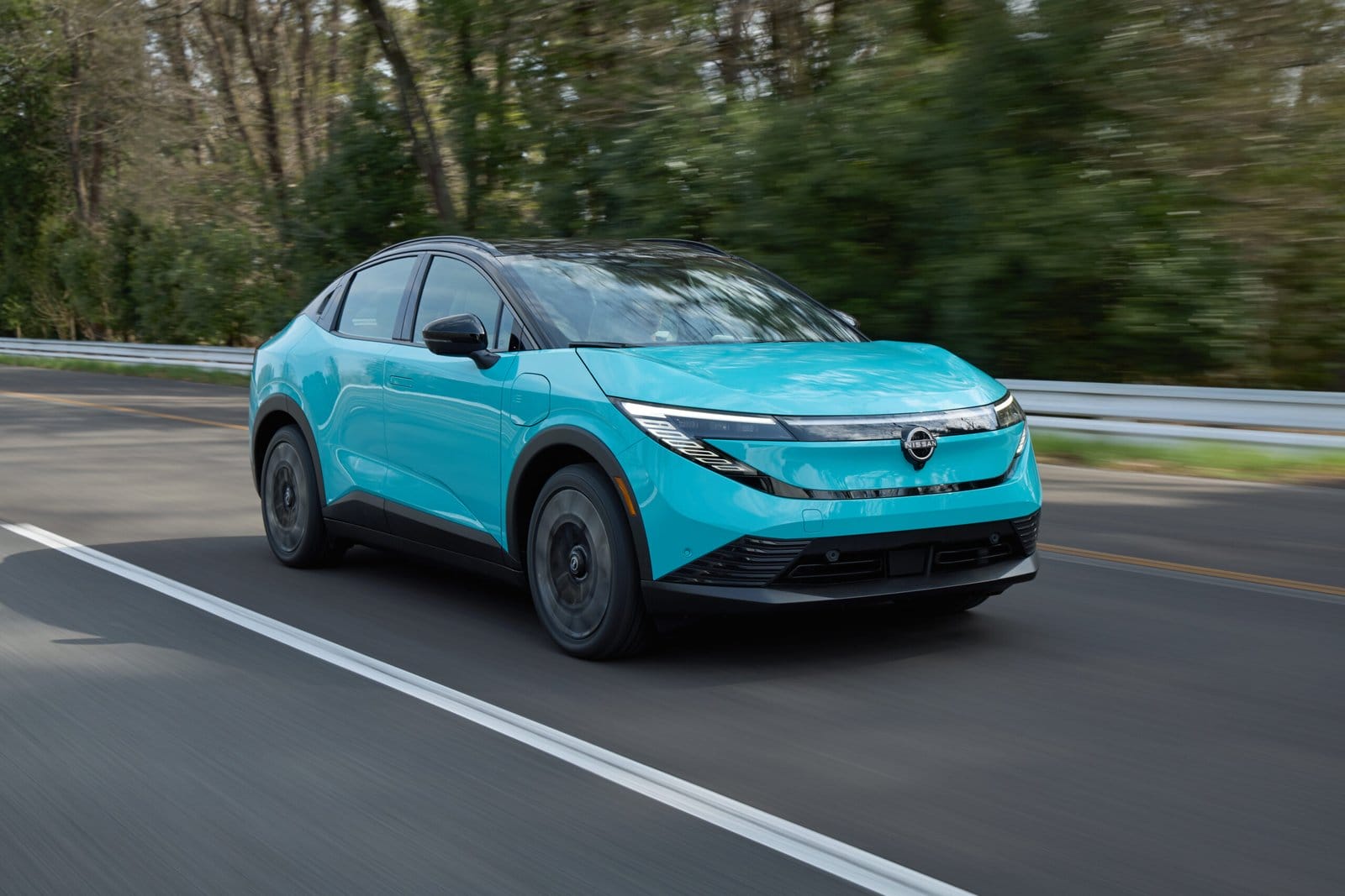 2025 Nissan Leaf electric vehicle driving on a two-lane road with trees in the background