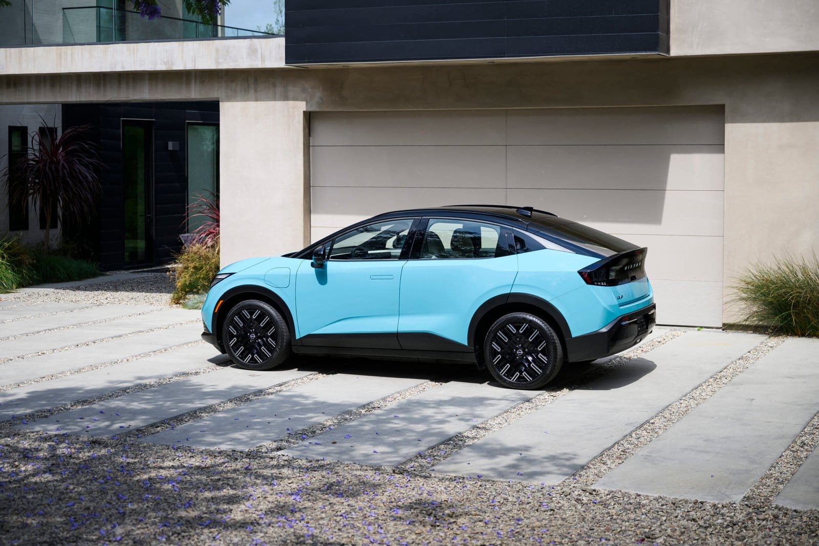 Blue Nissan Leaf electric vehicle parked in front of a modern home garage with a clean concrete and gravel driveway