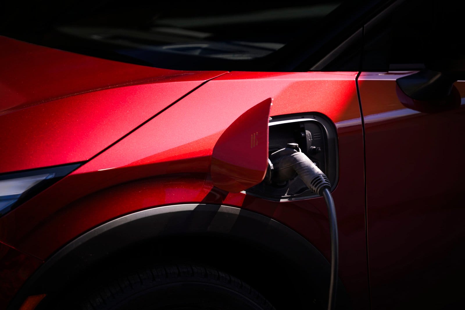 Close-up of a red Nissan Leaf electric vehicle charging with the cable connected to the front-side port
