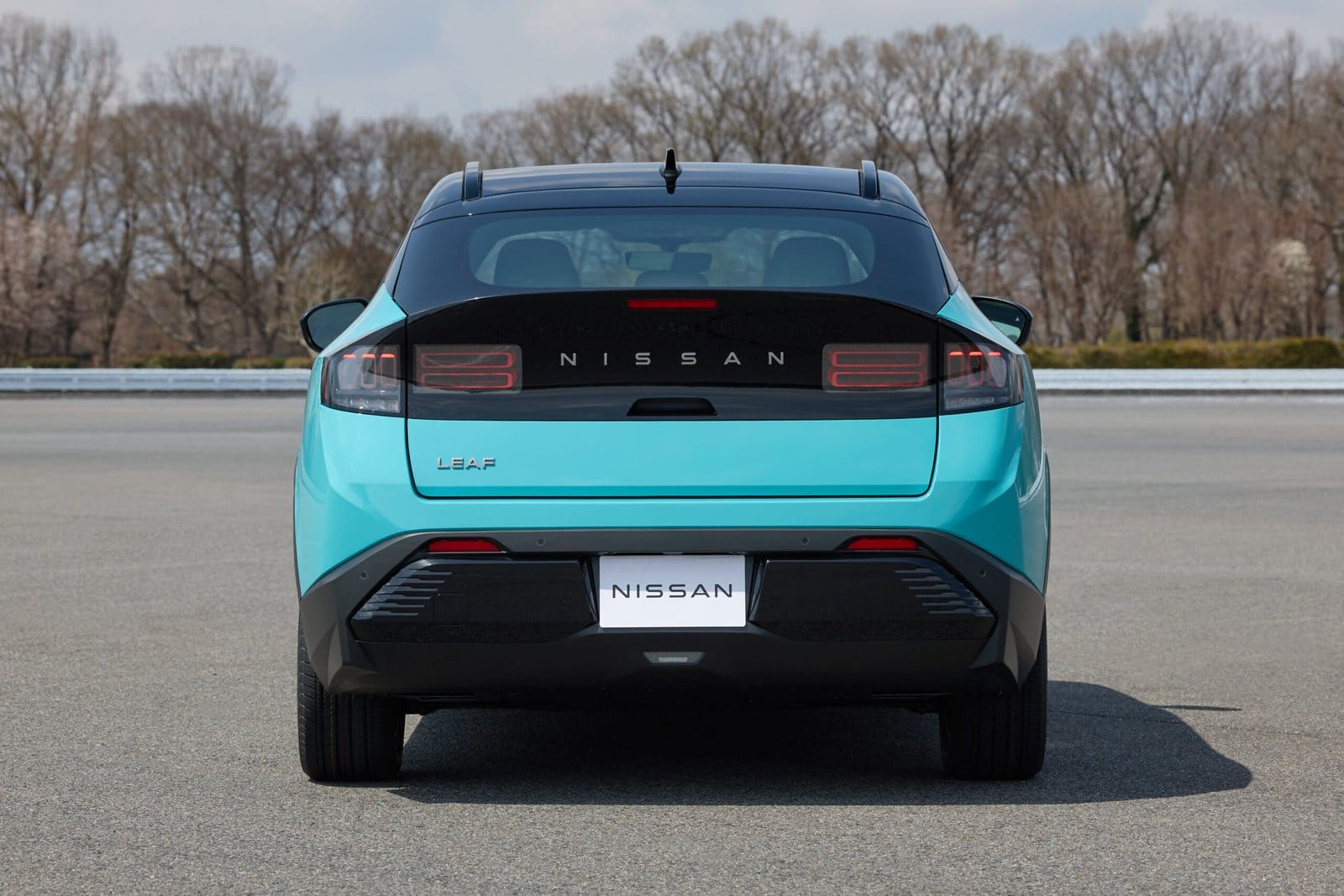 Nissan Leaf electric vehicle photographed from behind, showing taillights and rear bumper while parked on open pavement