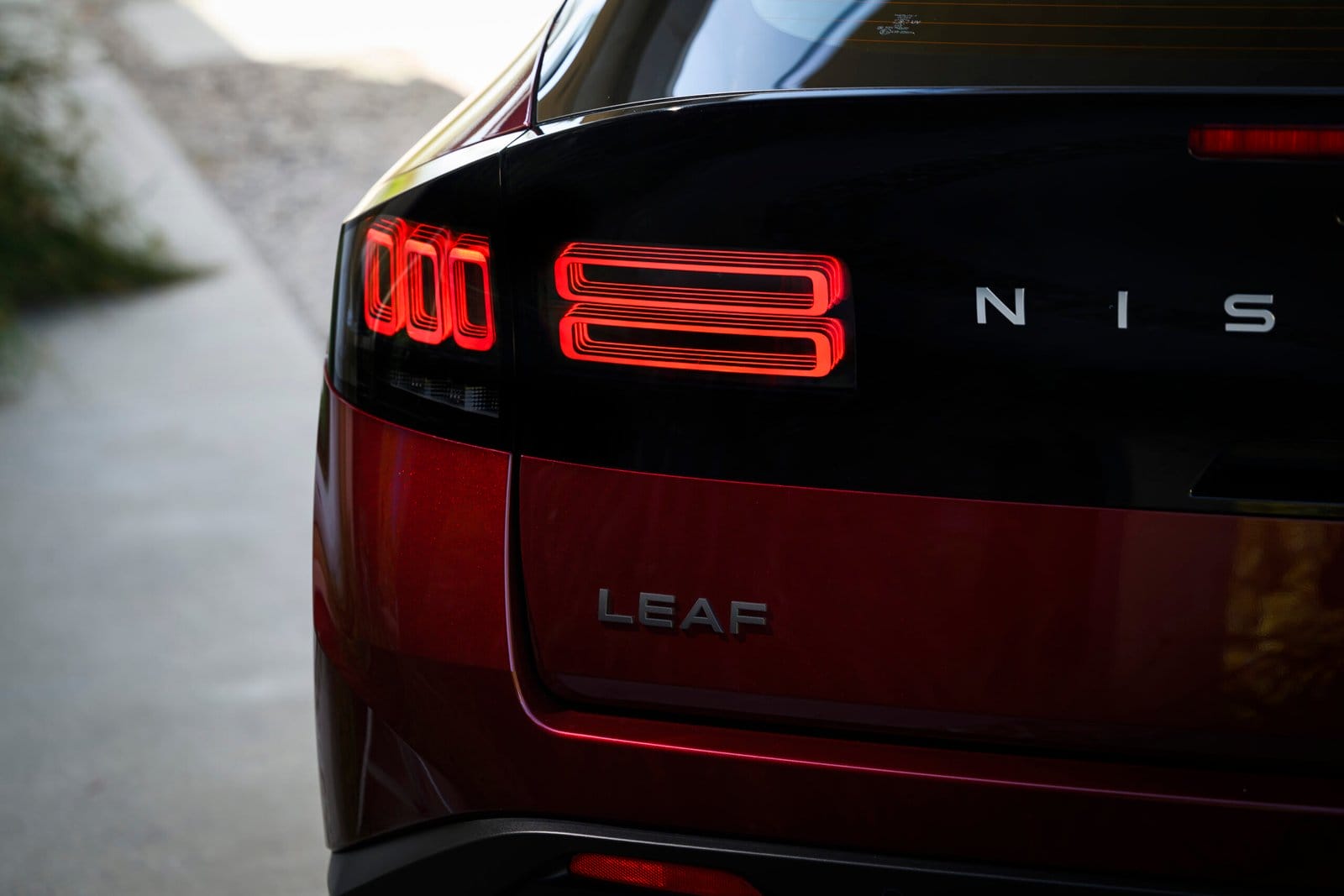 Close-up of the rear taillight and LEAF badge on a red Nissan Leaf electric vehicle with lights turned on