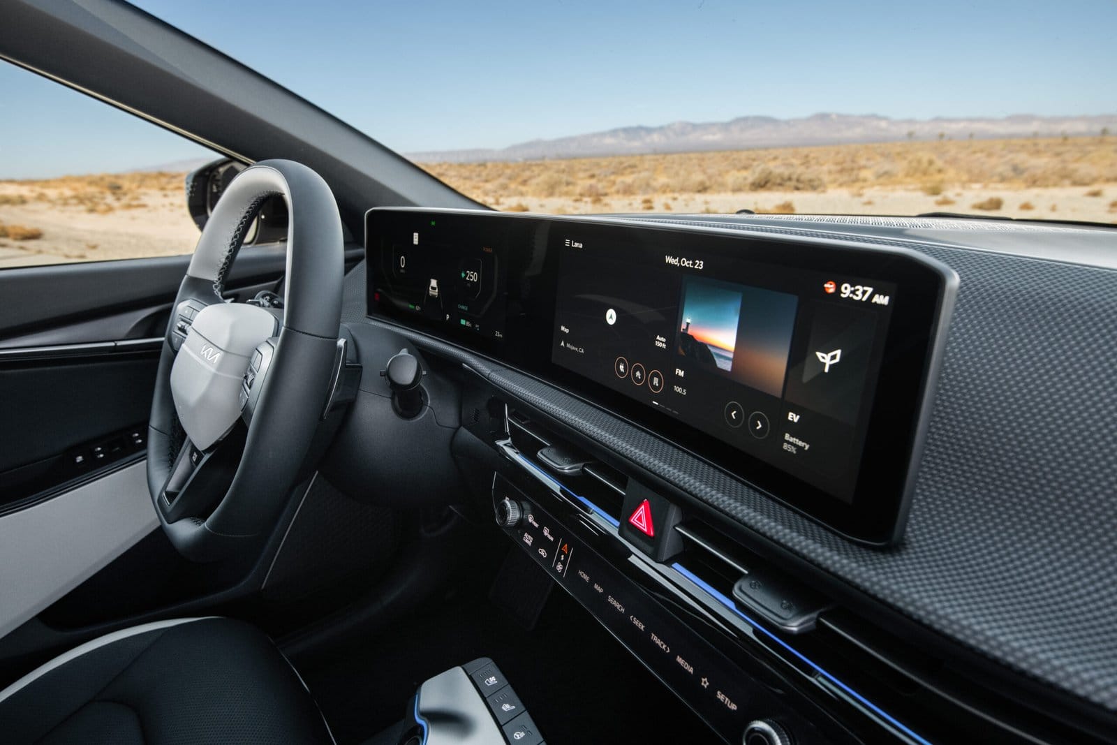 The interior of a Kia EV6 electric vehicle, showing a widescreen digital dashboard with driving data and media controls against a desert backdrop.