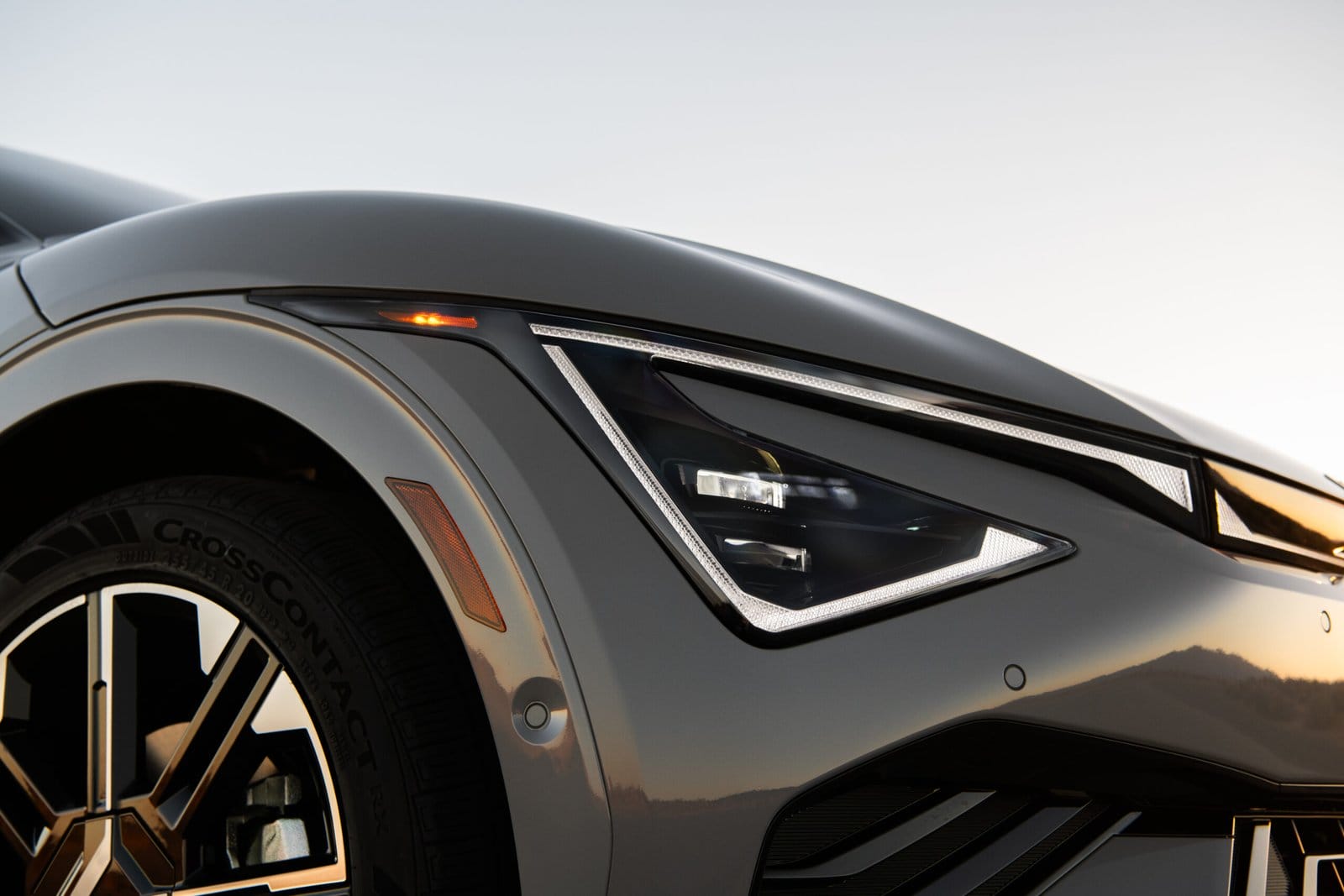 A detailed view of the Kia EV6 electric vehicle's headlight and front wheel, reflecting the sunset on its glossy surface.