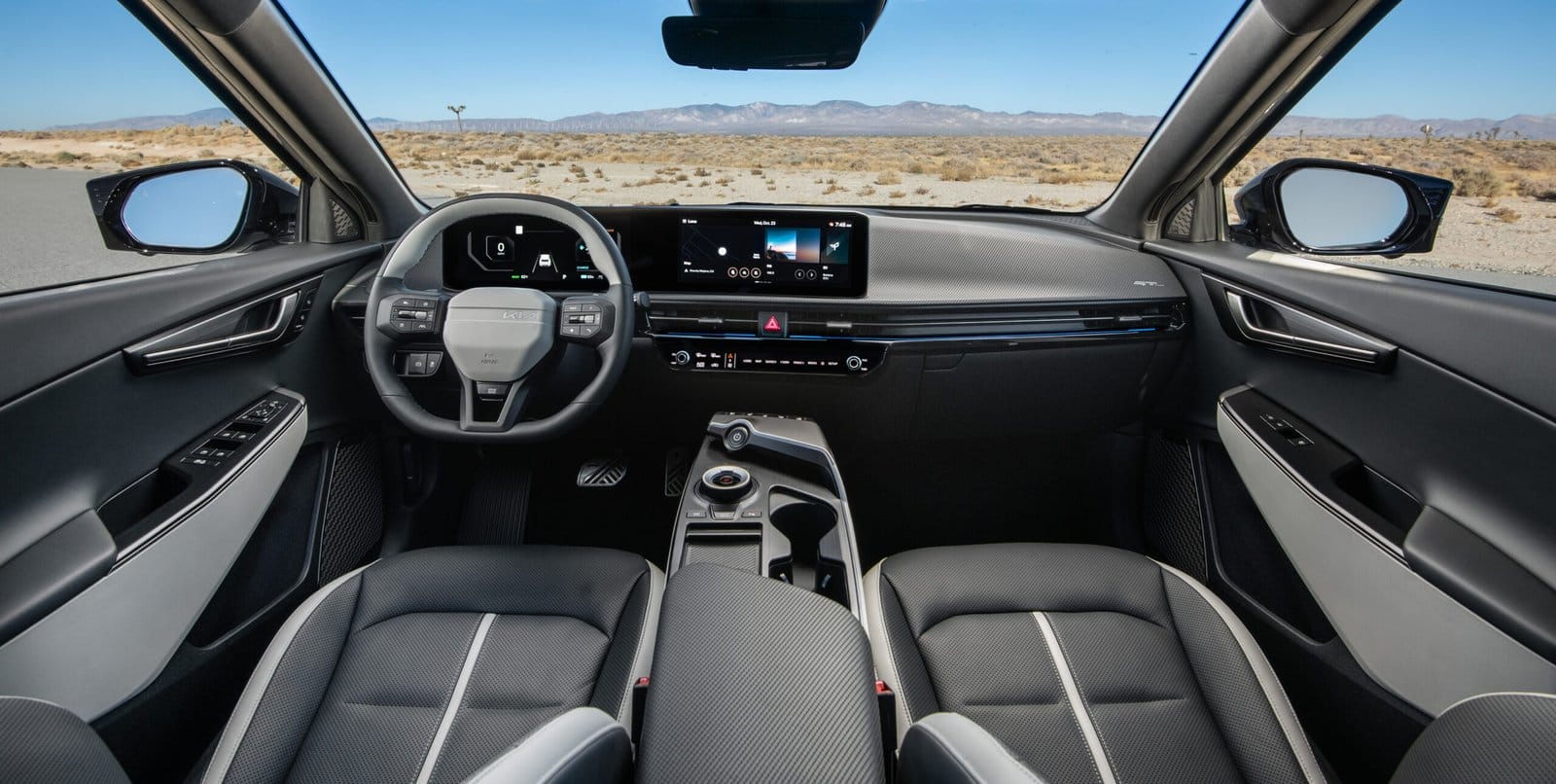 A full view of the Kia EV6 electric vehicle's modern interior, featuring a digital dashboard, steering wheel, and center console, with a desert landscape visible through the windshield.