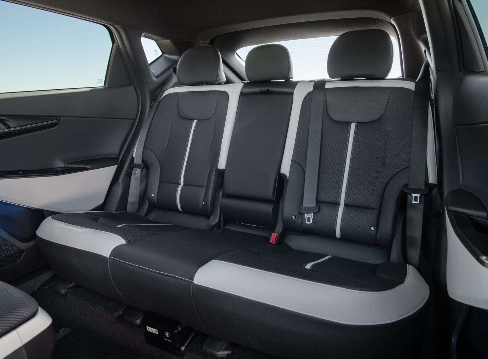 The back seats of the Kia EV6 electric vehicle, featuring black and white upholstery with three headrests and seat belts.