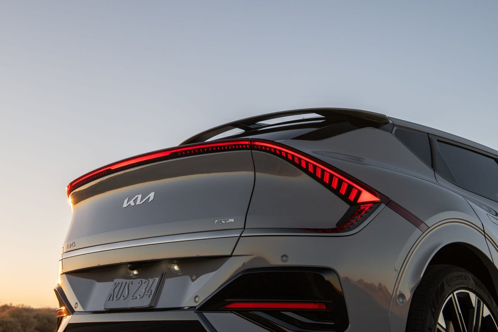 A close-up rear view of the Kia EV6 electric vehicle with illuminated taillights, captured at sunset against a clear sky.