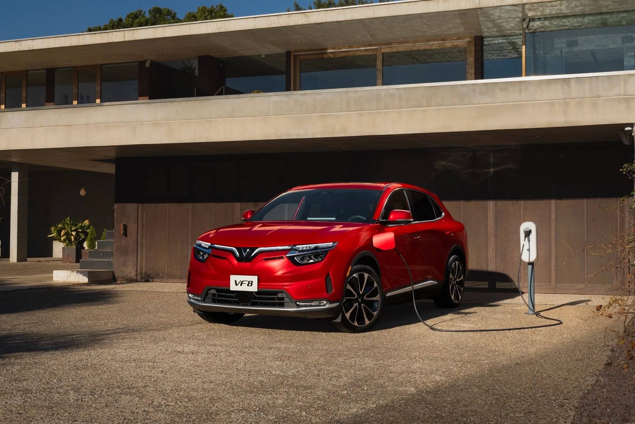 Red Vinfast VF8 electric vehicle plugged into a charging station outside a contemporary house