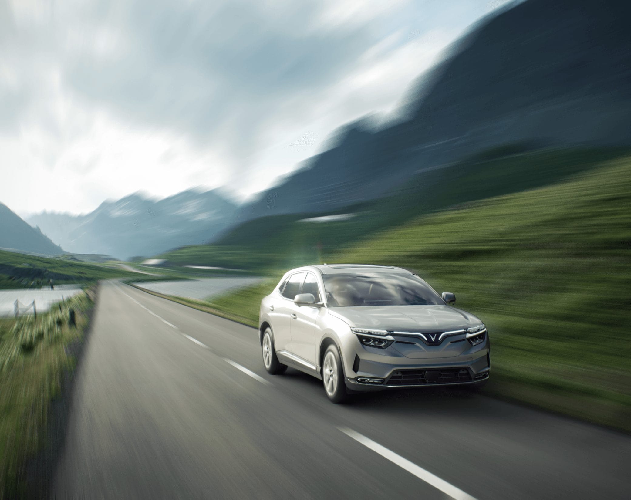 Vinfast VF8 electric vehicle in motion on a mountain road with lakes and green hills in the background