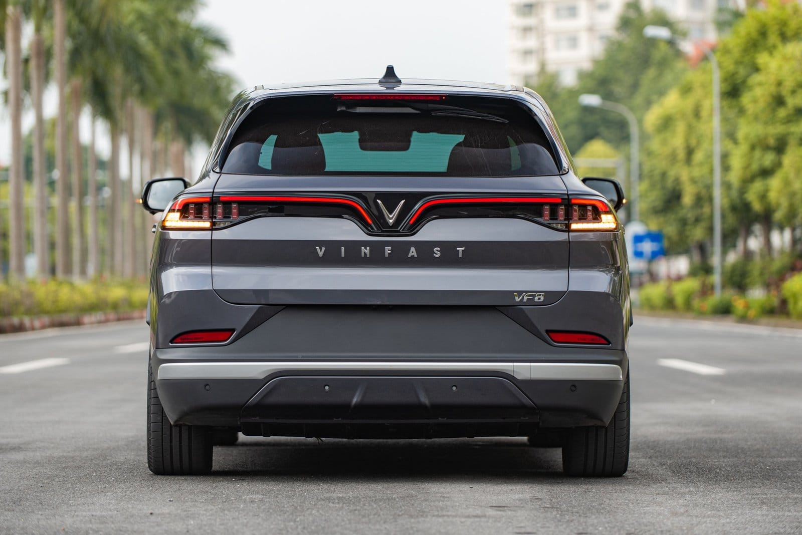 Back view of the Vinfast VF8 electric vehicle parked on a palm-lined urban street