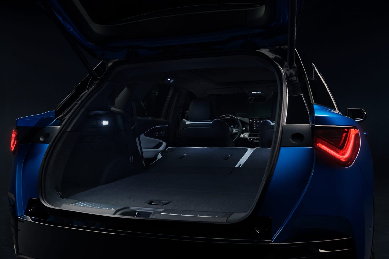 Rear view of the Acura ZDX electric vehicle showcasing its open trunk with folded rear seats, illuminated interior, and spacious cargo area.