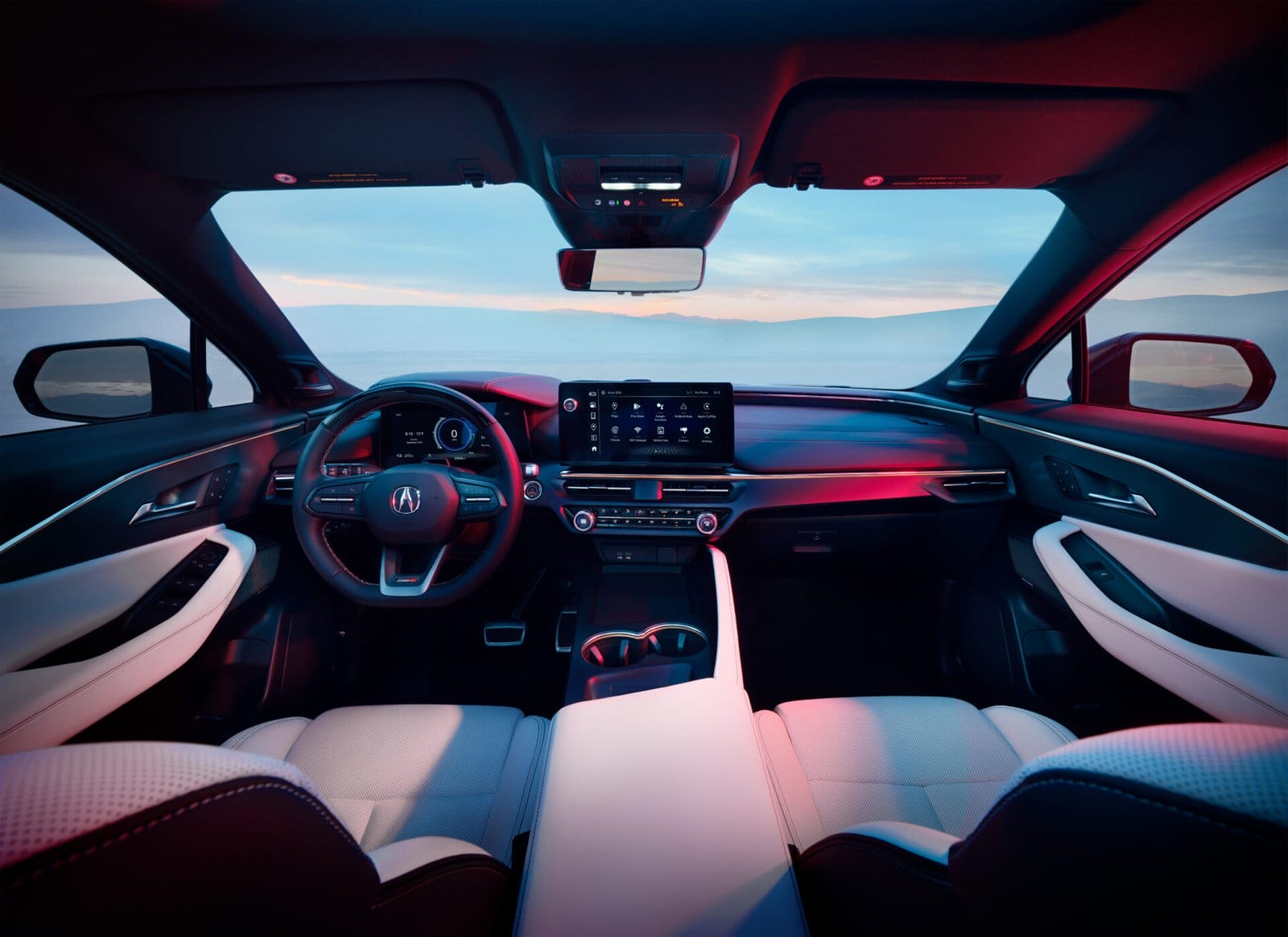 A view of the Acura ZDX electric vehicle's dashboard, steering wheel, and infotainment system from the driver’s seat, with a scenic outdoor backdrop visible through the windshield.
