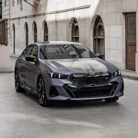 A silver BMW i5 electric vehicle parked on a narrow urban street, surrounded by classical building facades and soft lighting.