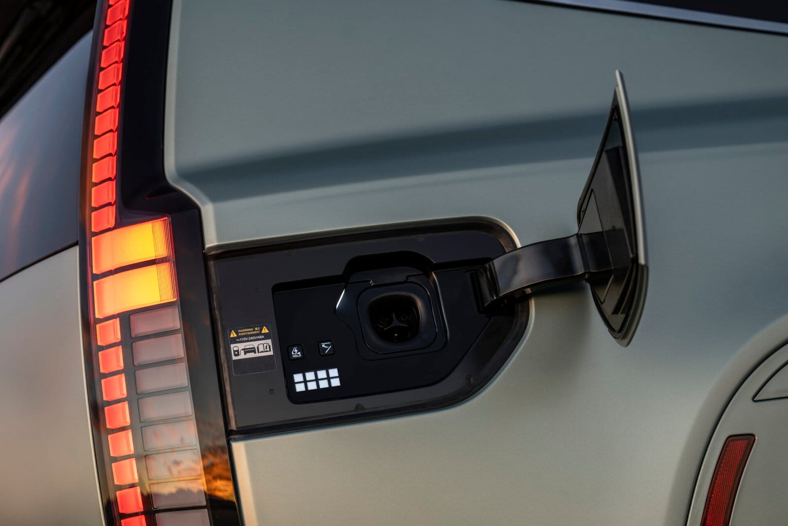 Close-up of the open charging port on the Hyundai Ioniq 9 electric vehicle, located near the tail light, with illuminated red accents and a soft evening light reflecting off the surface.