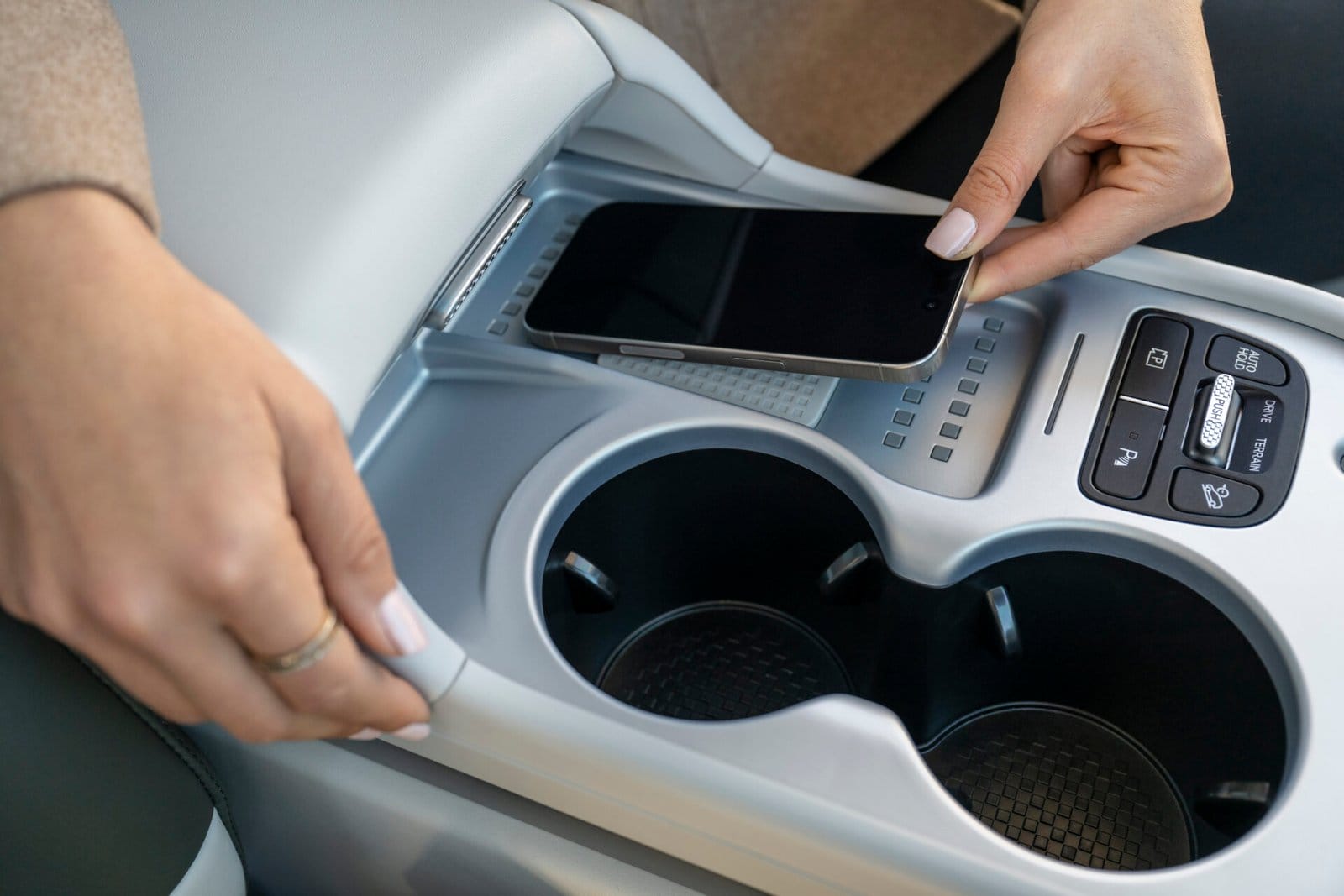 Close-up of a person placing a smartphone on the wireless charging pad in the Hyundai Ioniq 9 electric vehicle's center console, featuring cup holders and control buttons.