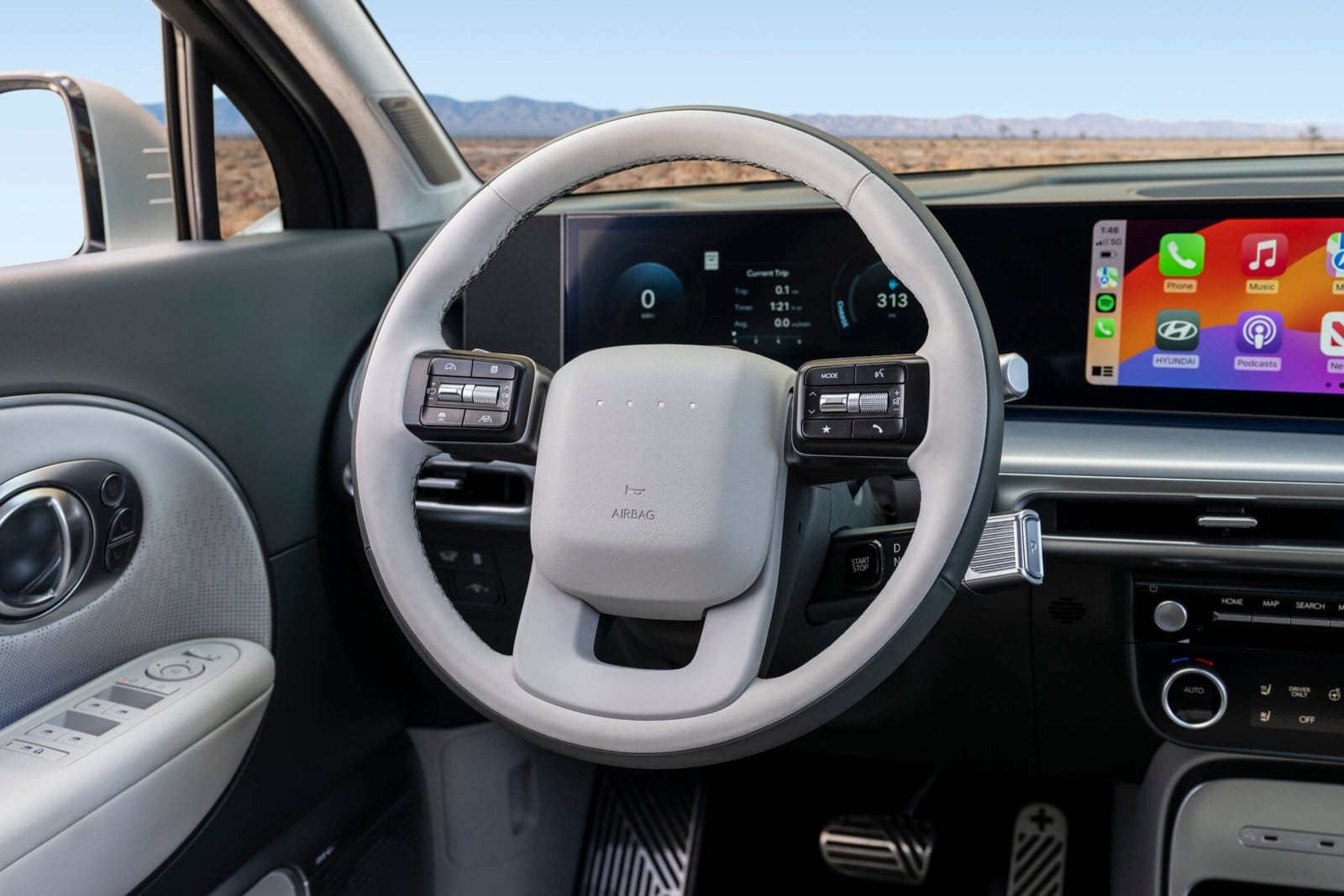 Close-up of the Hyundai Ioniq 9 electric vehicle's steering wheel with integrated controls, set against a dual-screen dashboard displaying driving metrics and infotainment features.