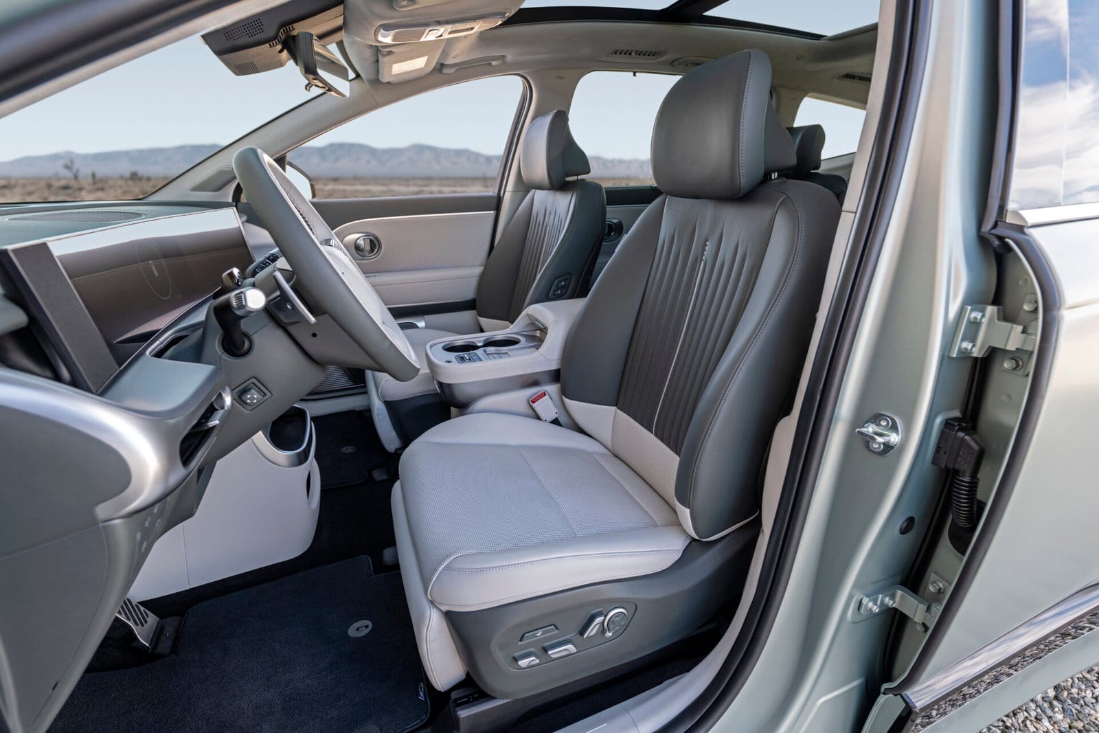 The front cabin of the Hyundai Ioniq 9 electric vehicle, showing two premium seats with gray and white upholstery, a panoramic sunroof, and a sleek dashboard design.