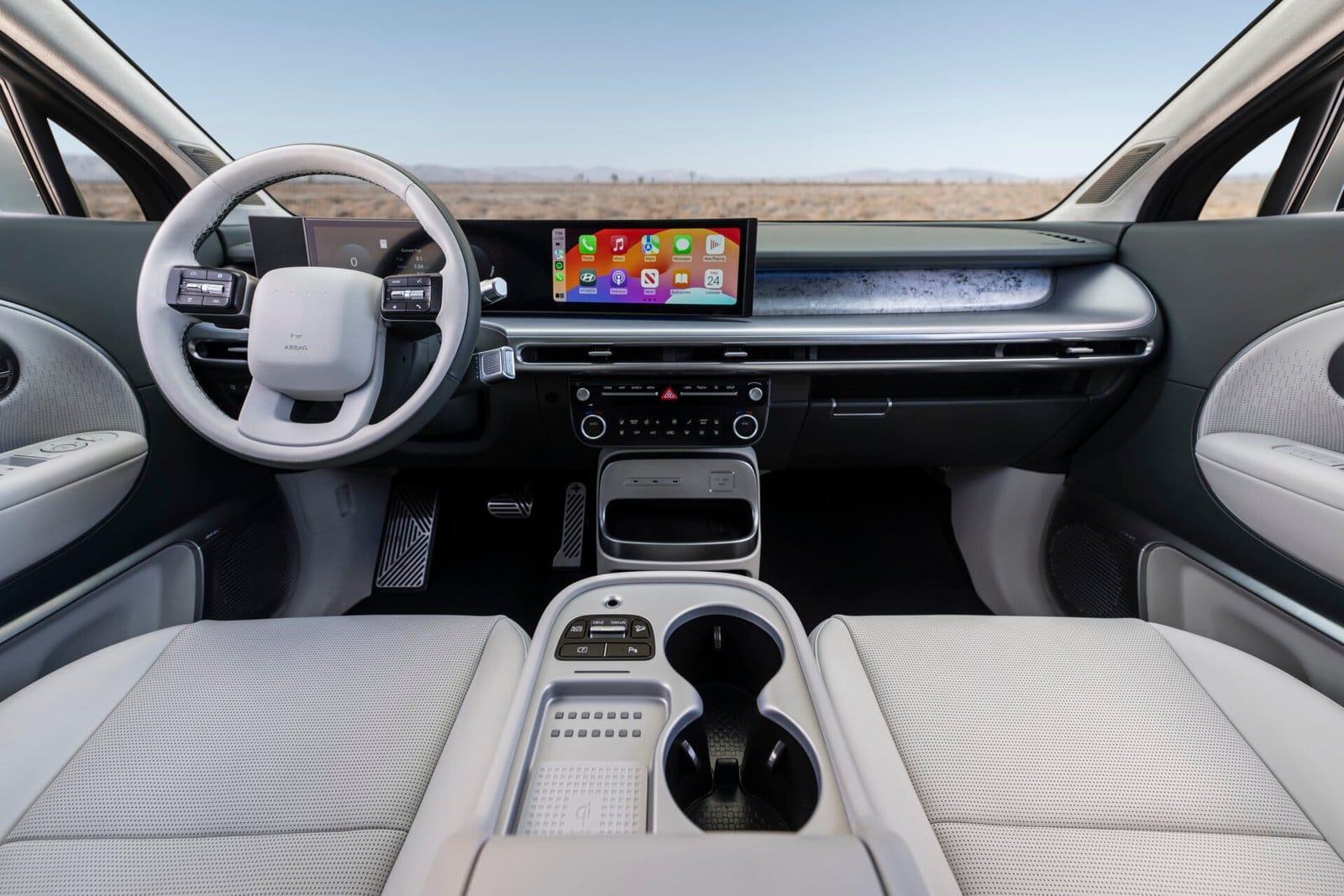 The Hyundai Ioniq 9 electric vehicle's interior, featuring a wide dashboard with a digital display, a steering wheel with integrated controls, and a center console with cup holders and a wireless charging pad.