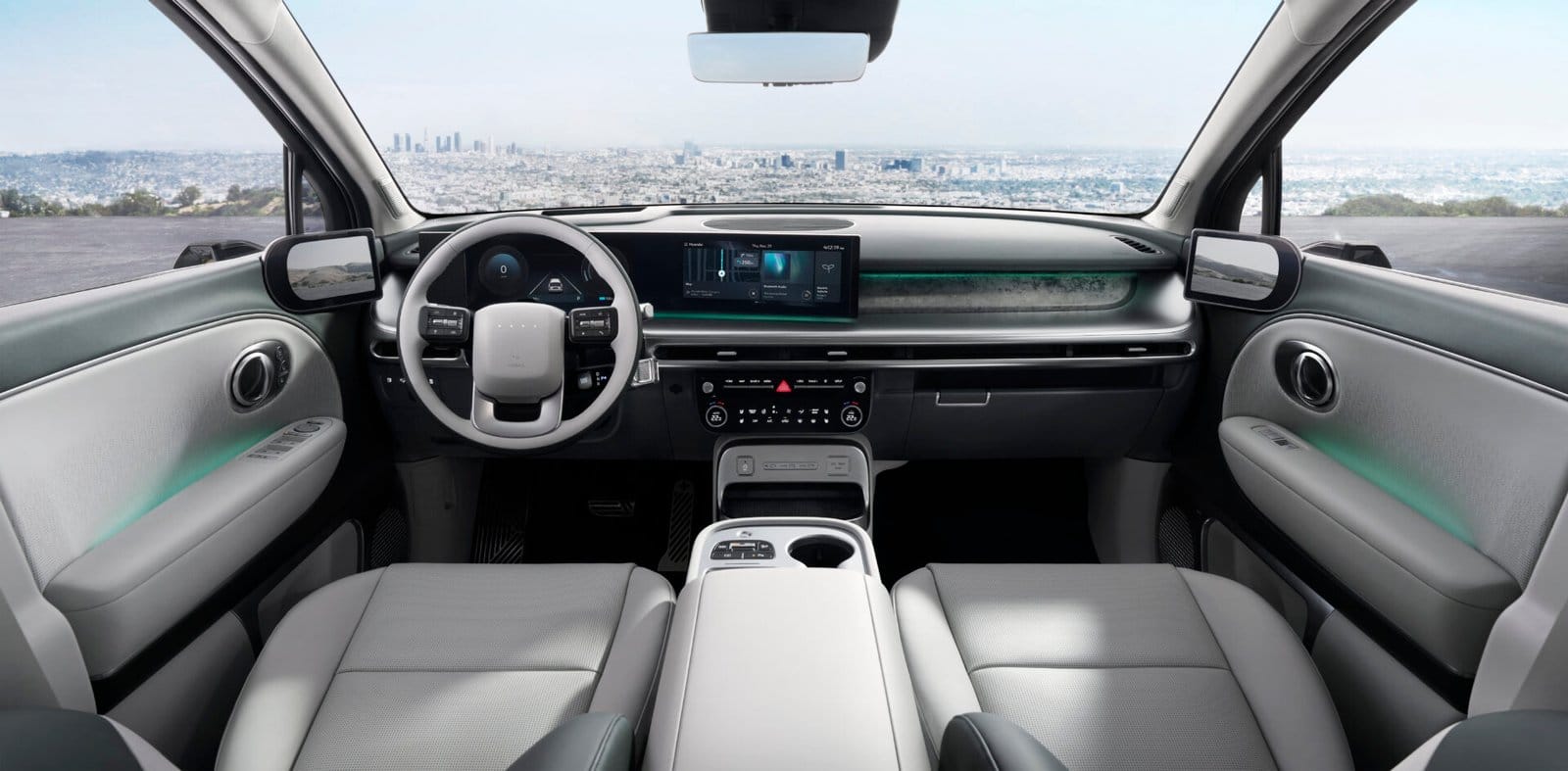 The interior of the Hyundai Ioniq 9 electric vehicle showcasing a sleek, modern design with a wide dashboard, digital displays, and light gray upholstery. A cityscape is visible through the windshield.
