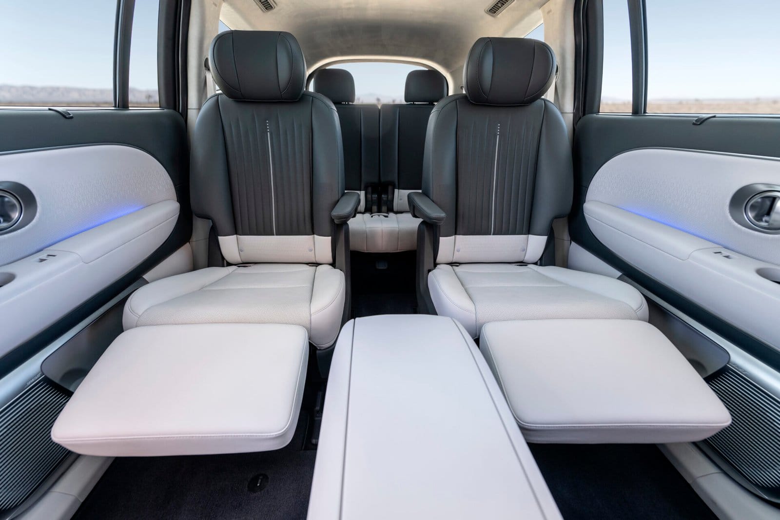 The rear cabin of the Hyundai Ioniq 9 electric vehicle, featuring two reclining captain’s chairs with light gray and black upholstery, adjustable leg rests, and ambient lighting.