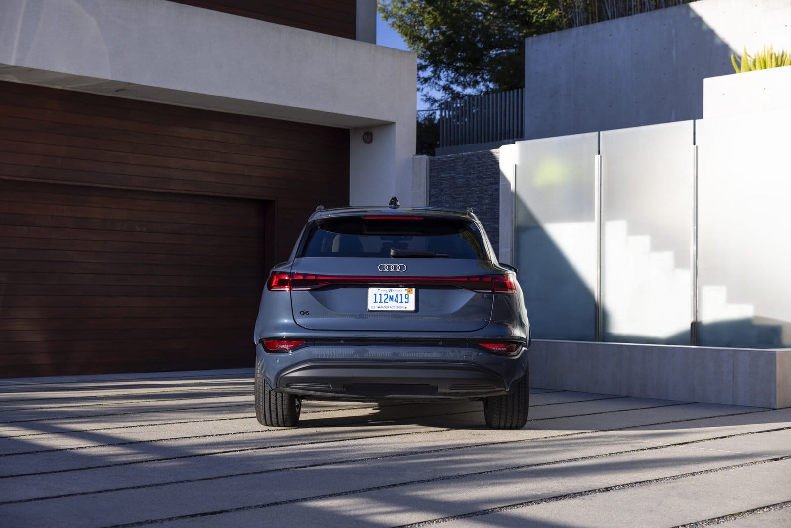 Rear view of blue Audi Q6 electric SUV with sleek taillights parked in modern residential driveway