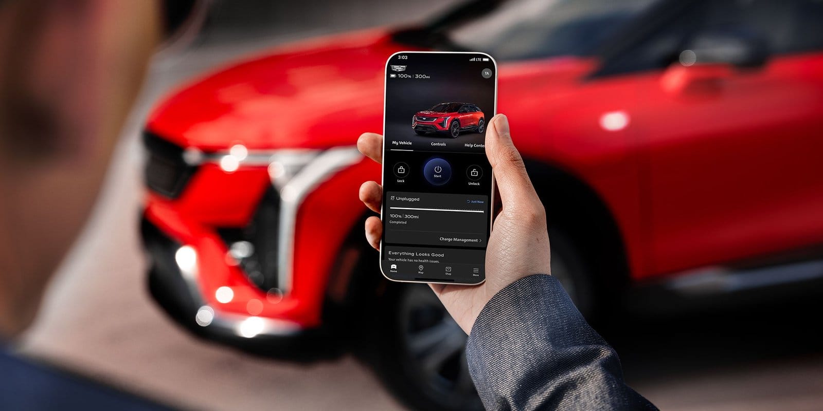 Person holding a smartphone showing Cadillac Optiq electric vehicle interface with battery status and remote functions