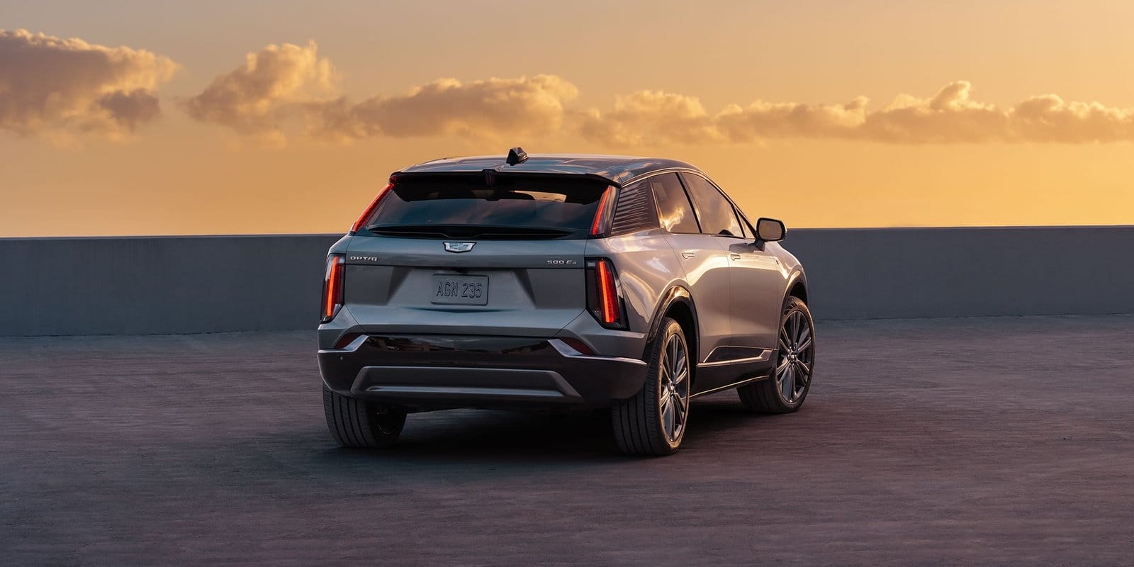 Sunset-lit rear passenger-side view of the Cadillac Optiq electric vehicle parked on a rooftop with visible 500E4 badge