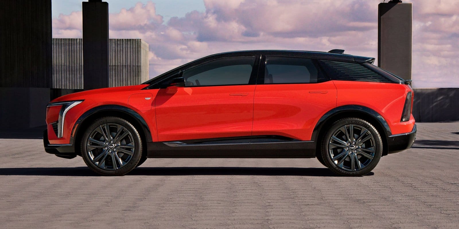 Side view of the red Cadillac Optiq electric vehicle parked in an open-air structure with concrete pillars