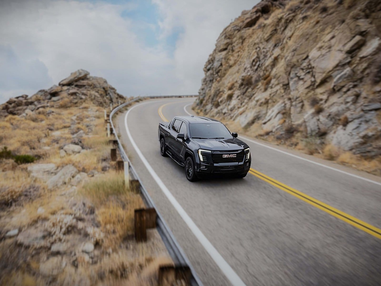 Black GMC Sierra EV electric vehicle navigating winding mountain road