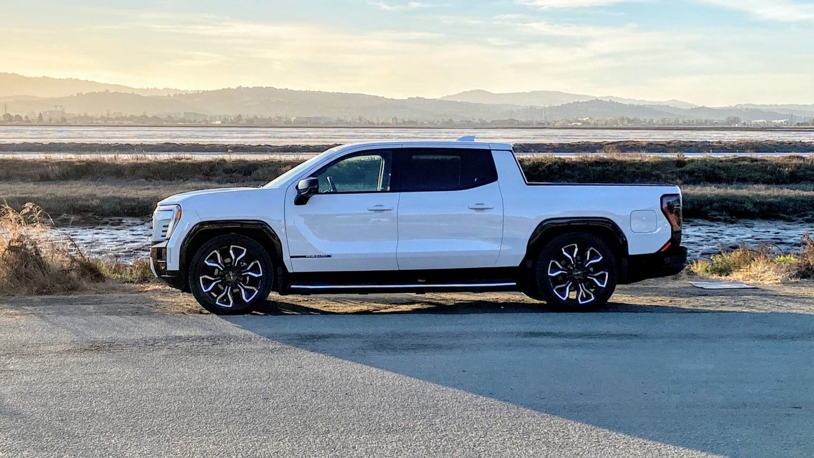GMC Sierra EV electric vehicle side view parked near water with mountains in the background