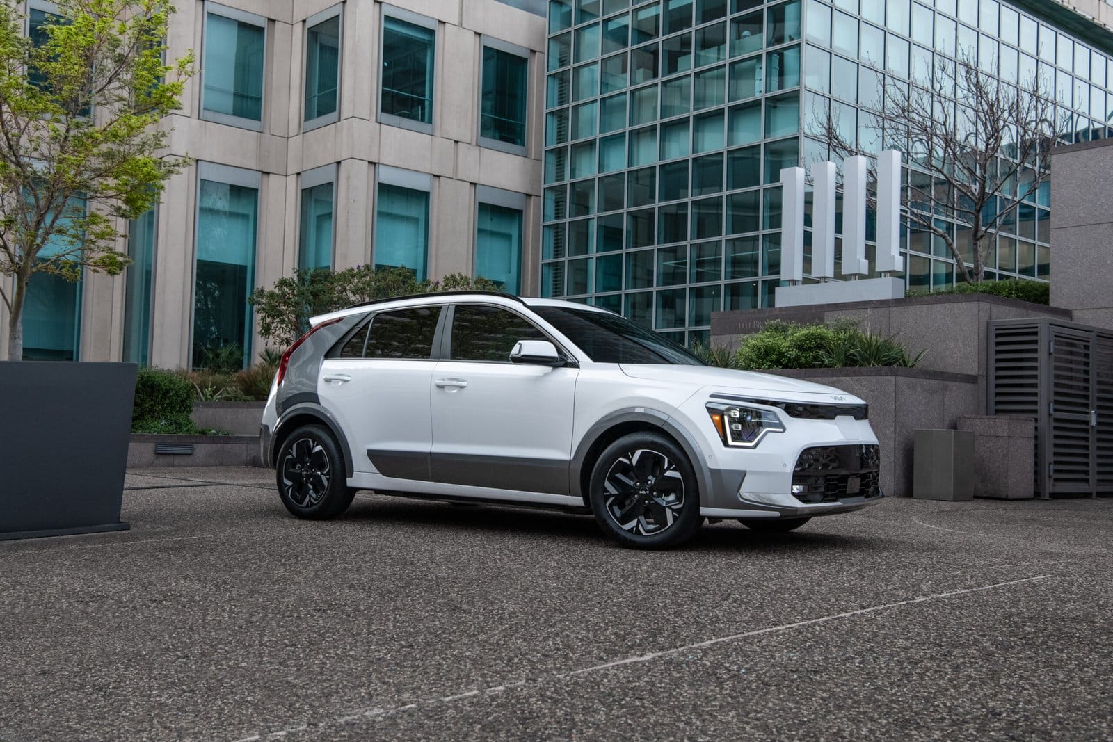 White Kia Niro EV electric vehicle parked in a city plaza with modern office buildings in the background