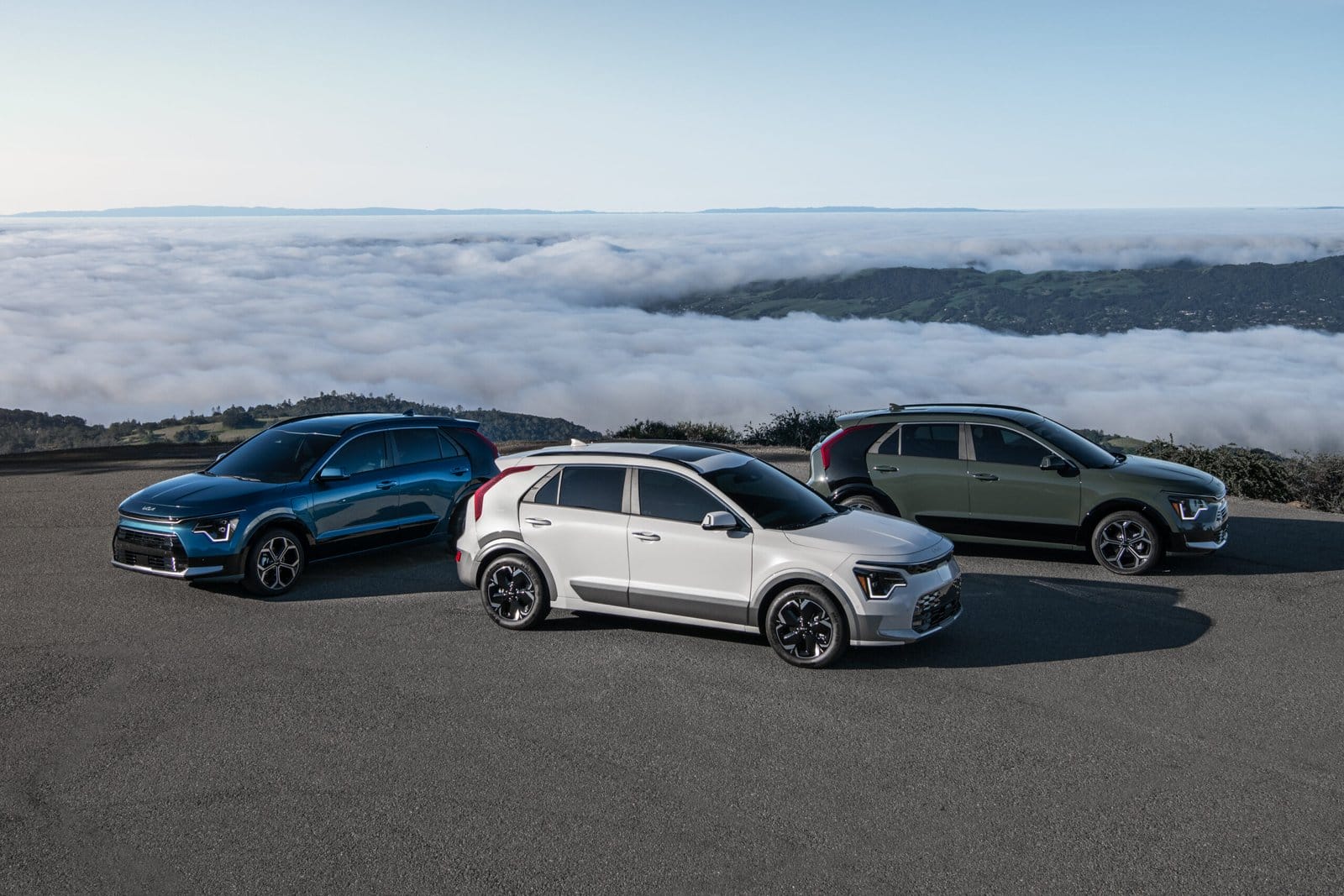 Three Kia Niro EV electric vehicles in different colors parked on a mountain road above the clouds