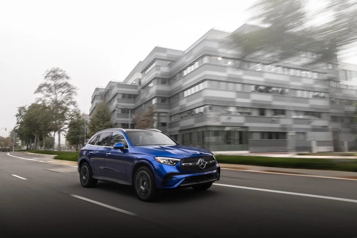 Blue Mercedes-Benz GLC PHEV electric vehicle driving on an empty urban road with modern buildings in the background