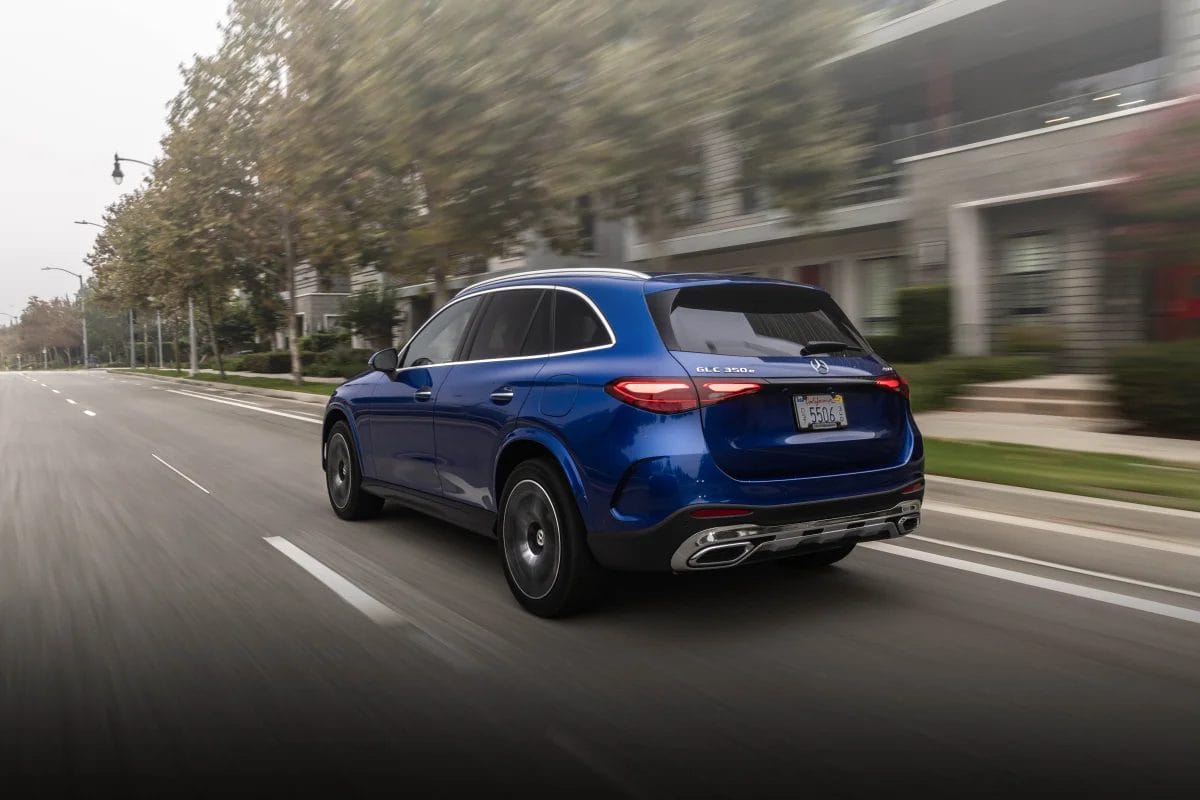Rear view of a blue Mercedes-Benz GLC PHEV electric vehicle driving down a tree-lined city street