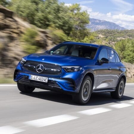Blue 2025 Mercedes-Benz GLC 350e electric vehicle driving on a scenic road with hills and trees in the background