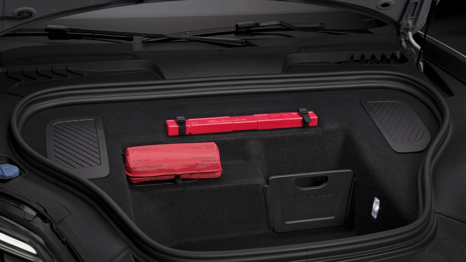 Front trunk (frunk) of the Porsche Macan EV electric vehicle showing storage area with safety equipment and molded compartments