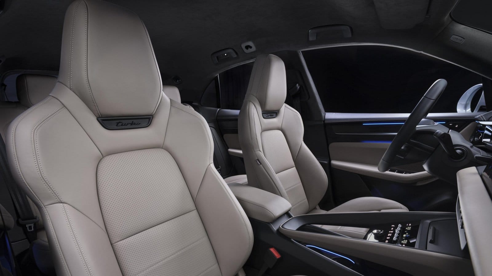 Front sport seats of the Porsche Macan EV electric vehicle featuring Turbo branding, beige leather upholstery, and ambient-lit cabin