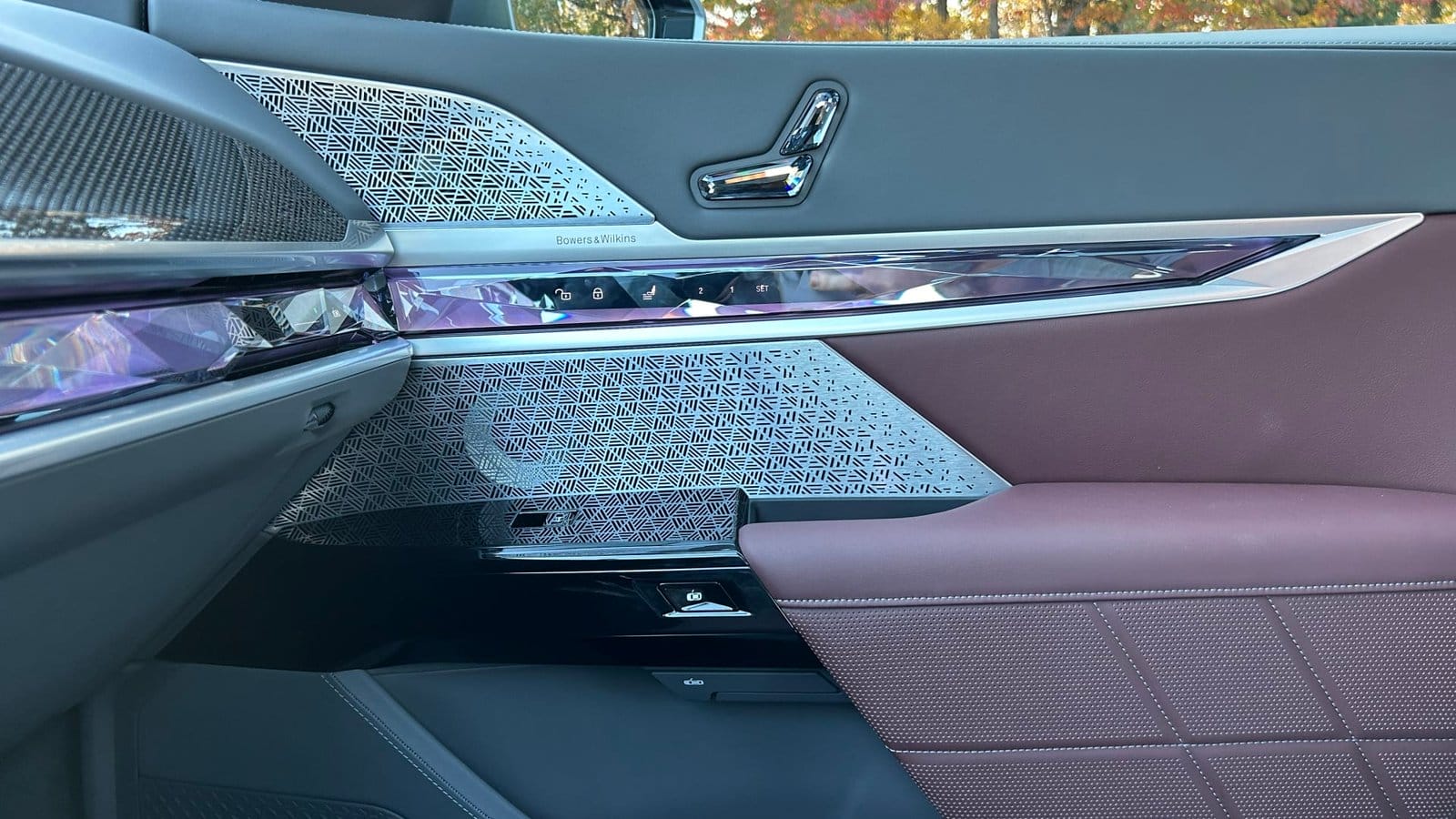 Close-up of front door panel in BMW 750e xDrive Plug-in Hybrid vehicle showing seat controls, Bowers & Wilkins speaker grille, and ambient lighting