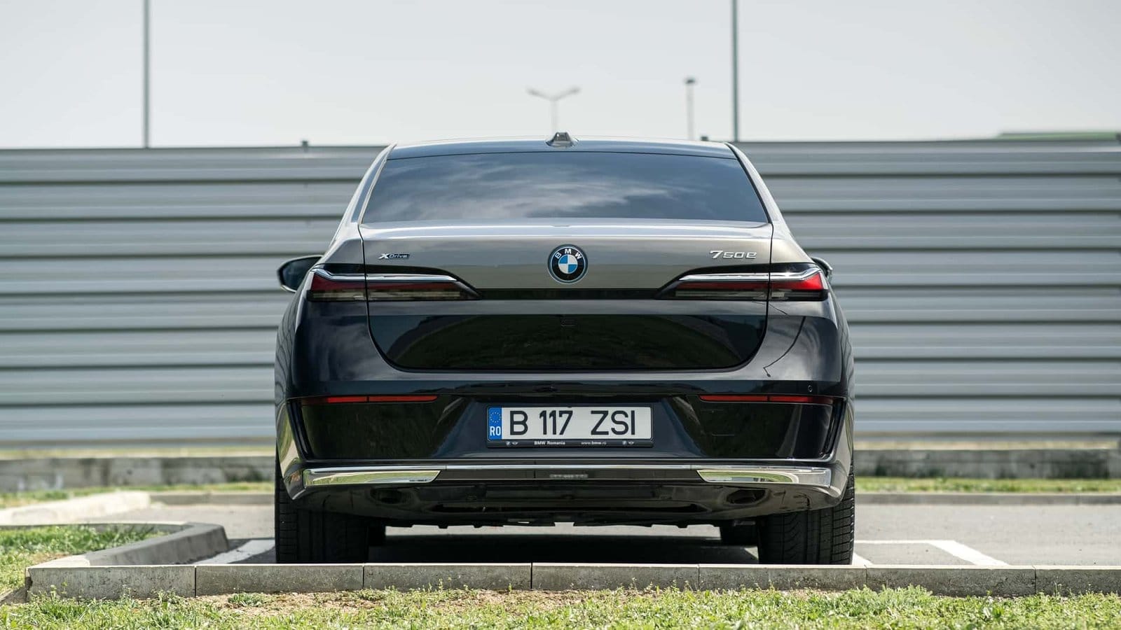 Straight-on rear view of a black BMW 750e xDrive Plug-in Hybrid vehicle with Romanian license plate, parked on a curb