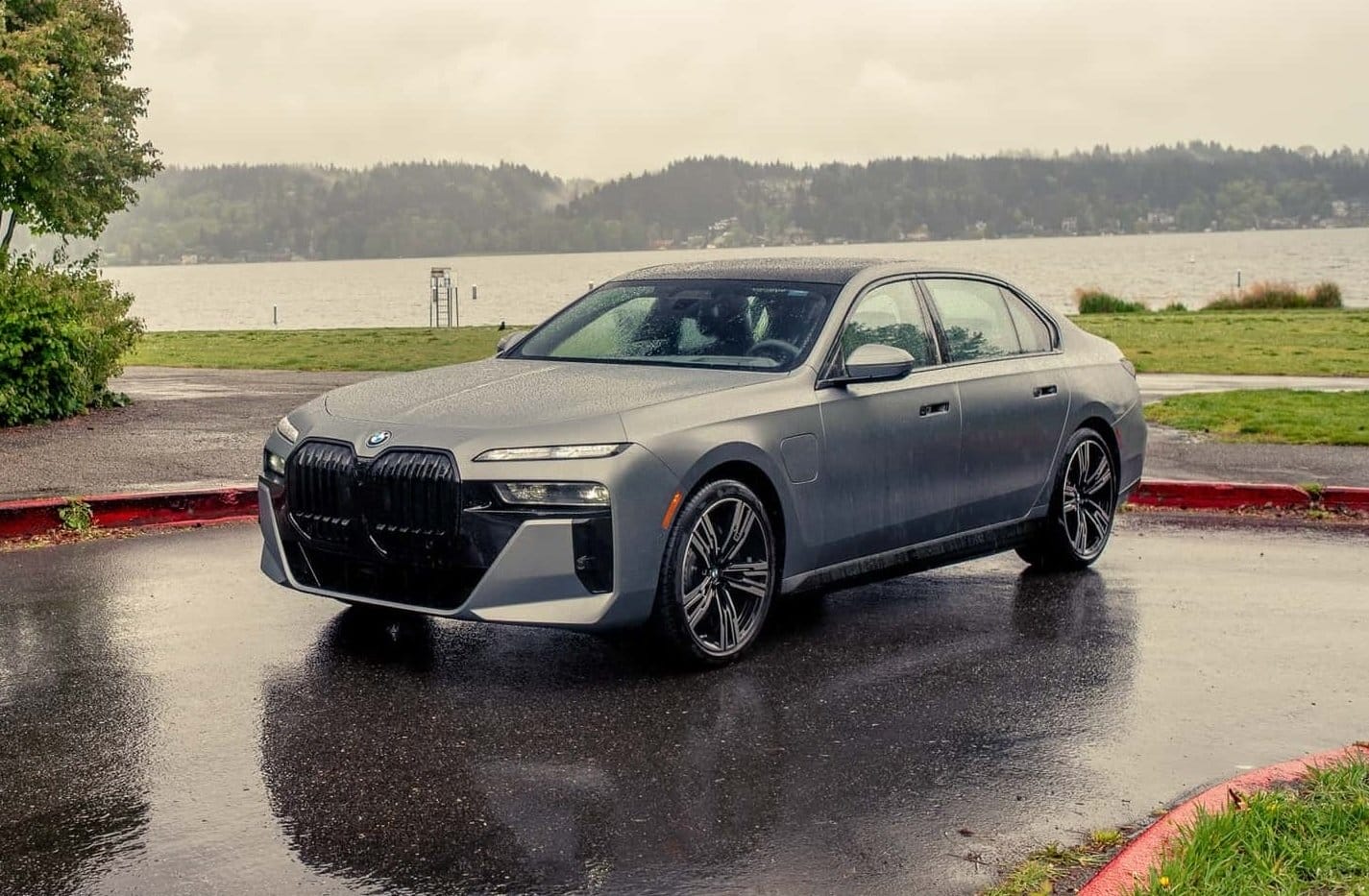 BMW 750e xDrive Plug-in Hybrid parked near a lake on a rainy day with wet pavement and cloudy sky