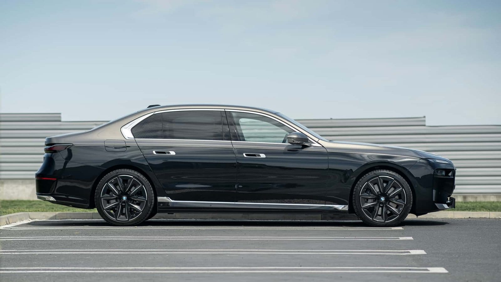 Full side view of a black BMW 750e xDrive Plug-in Hybrid vehicle parked in an empty lot with modern fencing in the background