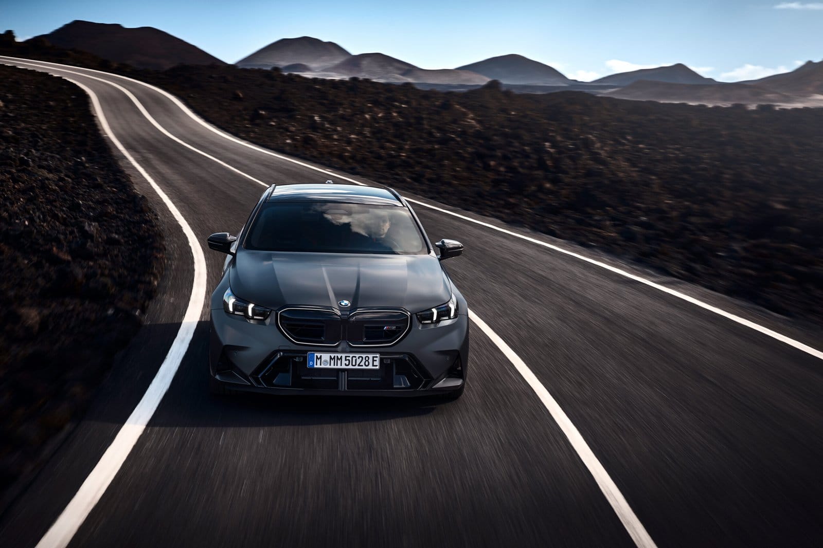 Front view of the 2025 BMW M5 Touring Plug-in Hybrid driving on winding road through volcanic landscape