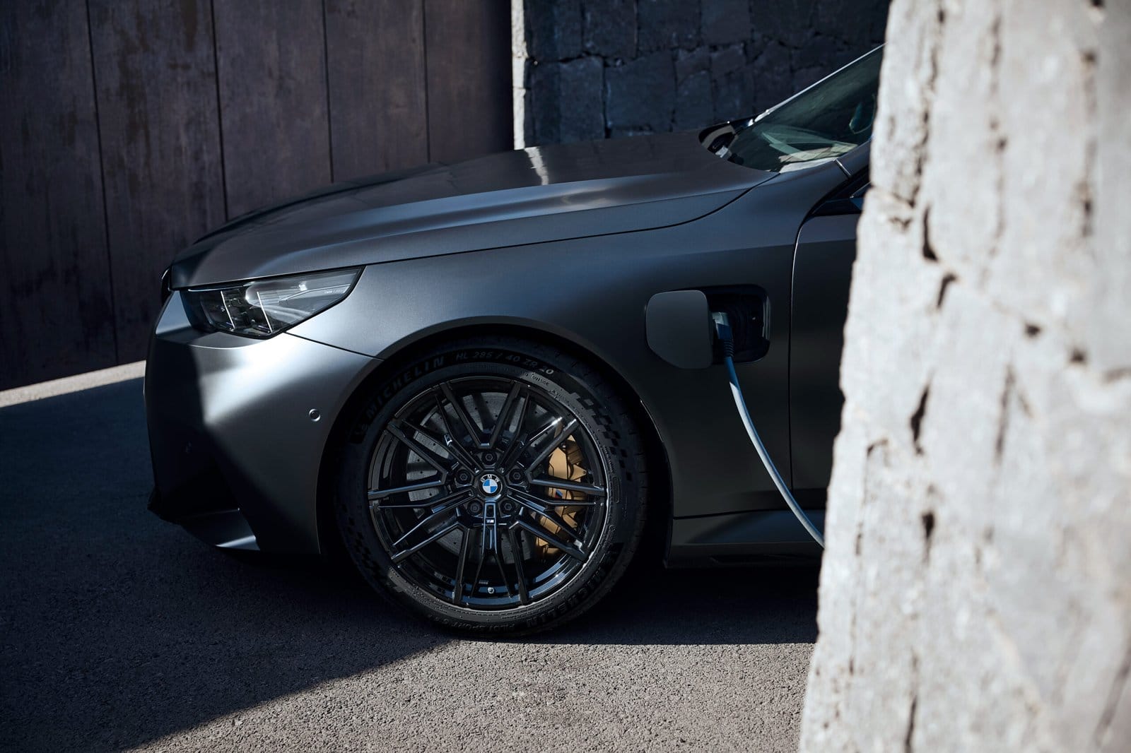 Front wheel and headlight view of BMW M5 Touring Plug-in Hybrid charging with cable connected to the fender port