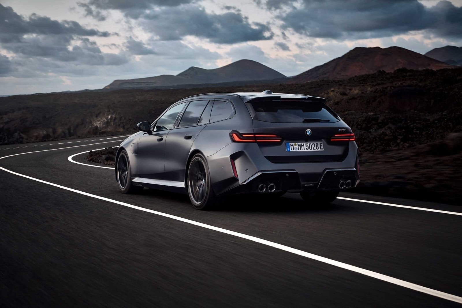 Rear three-quarter view of BMW M5 Touring Plug-in Hybrid driving on a winding mountain road at dusk