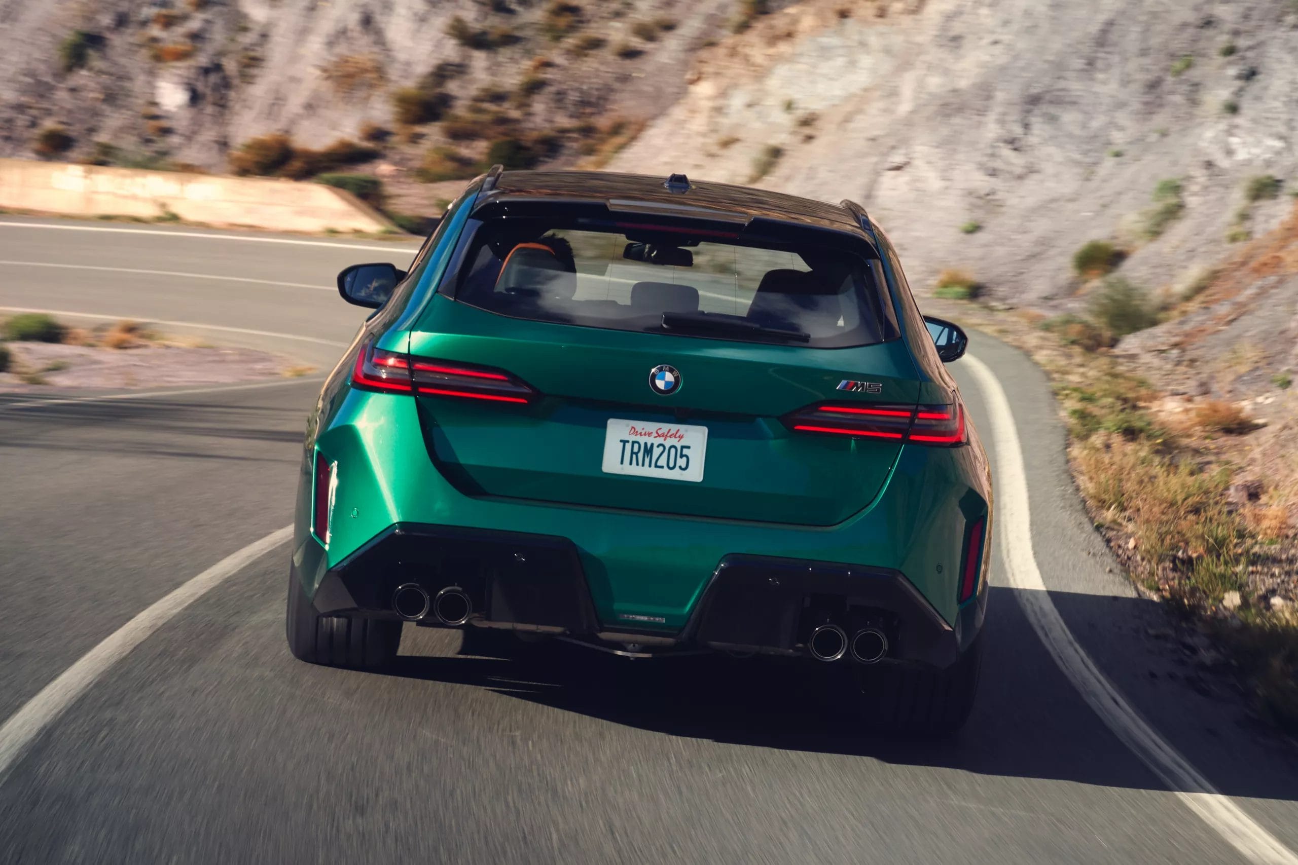 BMW M5 Touring Plug-in Hybrid viewed from the rear while driving on a winding road through rocky terrain