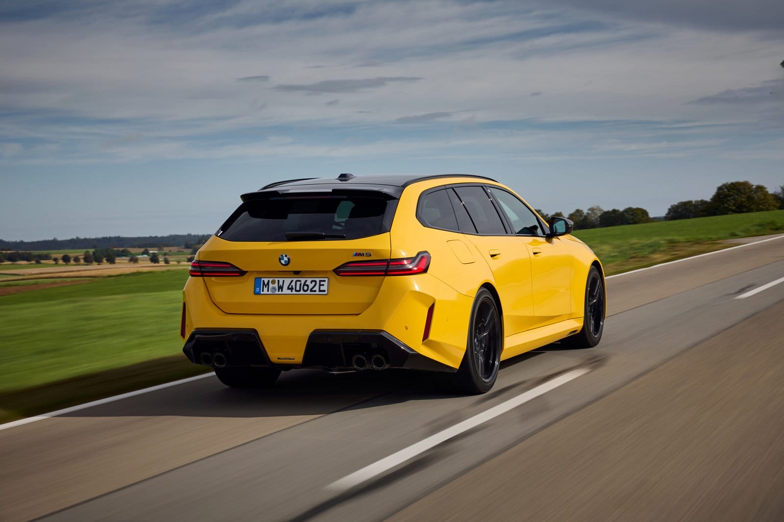 Yellow 2025 BMW M5 Touring Plug-in Hybrid seen from the rear side driving on a country road